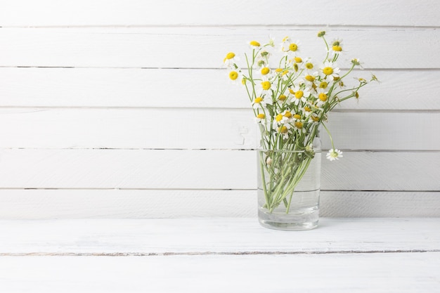 Bouquet of chamomiles in a glass vase on wooden background