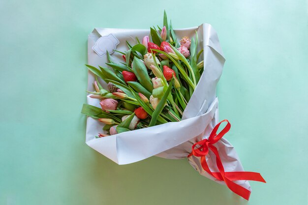 Bouquet of chocolate covered strawberries and tulips on green background