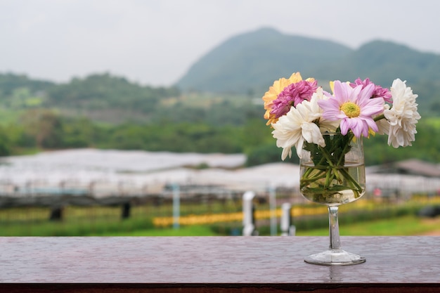 山の背景と木製のテーブル上のガラス瓶の菊の花束