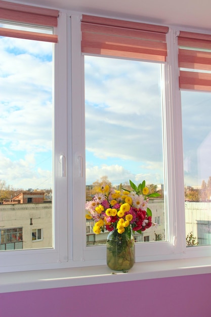 Bouquet of chrysanthemums stands on windowsill in front of window Beautiful flowers in bouquet by window on windowsill Room design element Interior of modern loggia