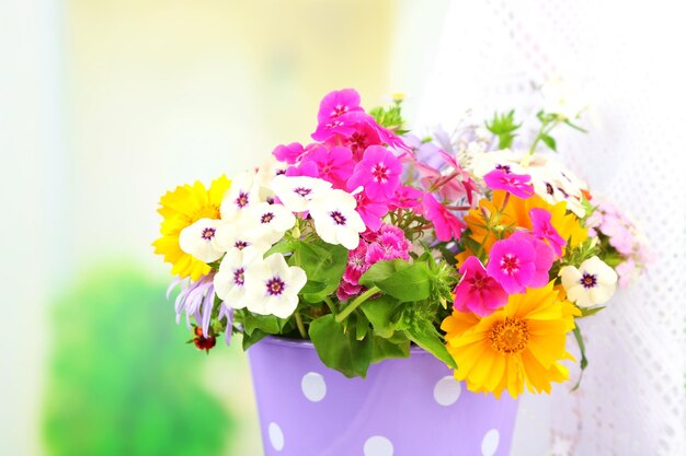 Bouquet of colorful flowers in decorative bucket on chair on bright background