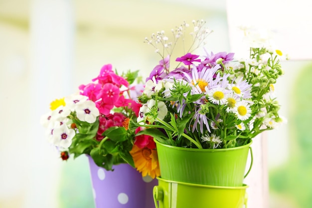 Bouquet of colorful flowers in decorative buckets on chair on bright background