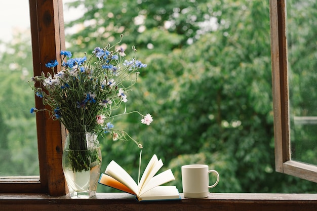 Photo a bouquet of cornflowers and a book on the windowsill in a cozy home