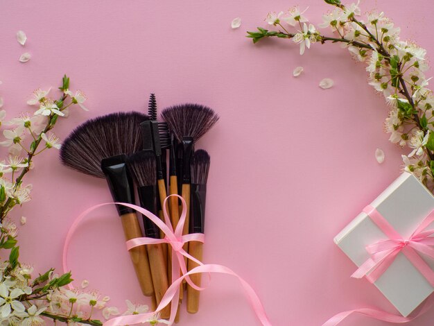 Bouquet of cosmetic brushes tied with a ribbon with a bow on pink background