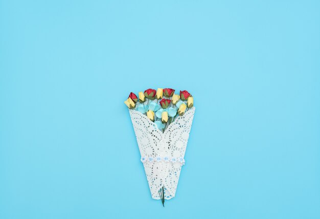 The bouquet of craft flowers wrapped in a white lace bundle on blue background.