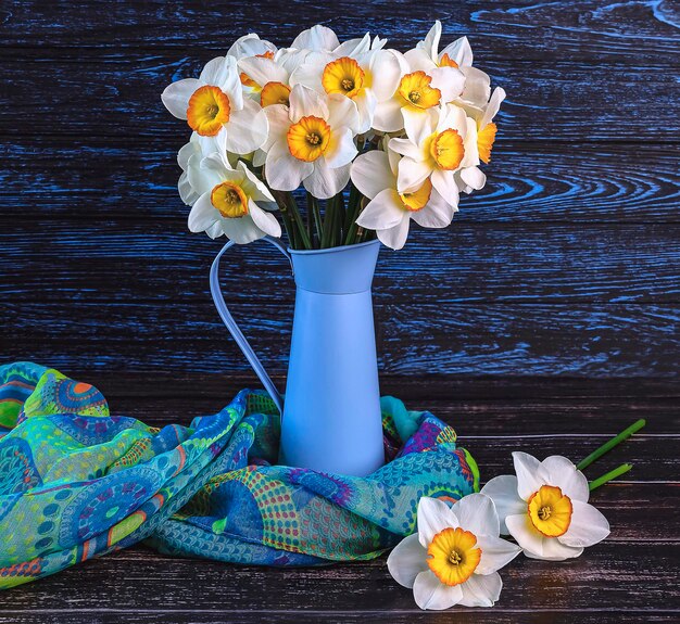 Photo bouquet of daffodils flowers in blue vase colorful shawl on dark wooden background