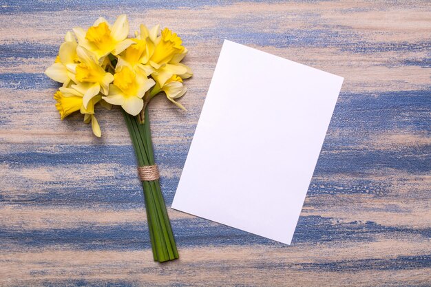 A bouquet of daffodils and a sheet of white paper on a wooden background