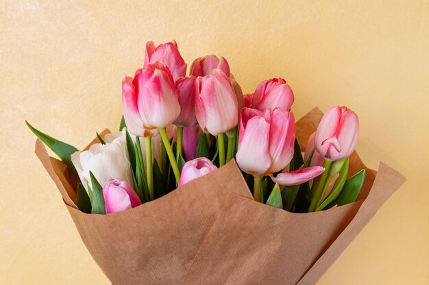 Foto bouquet di delicati tulipani rosa e bianchi in carta artigianale su uno sfondo giallo chiaro