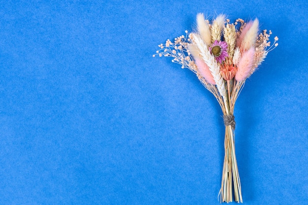 Bouquet of dried flower and spikelets lies on blue