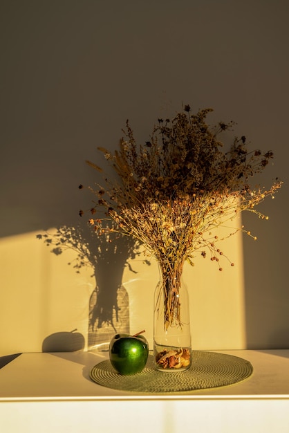 Bouquet of dried flowers on the table in a glass vase, in the\
light of the sun, contrasting image