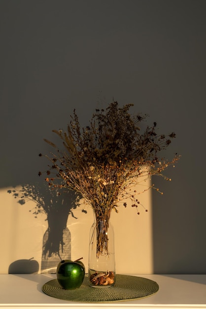 Bouquet of dried flowers on the table in a glass vase, in the\
light of the sun, contrasting image