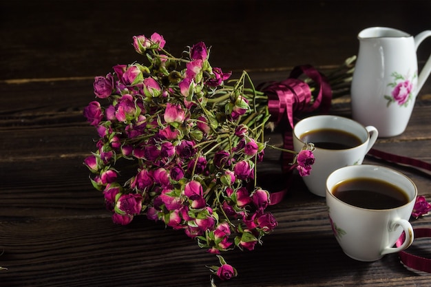 暗い木の表面にリボンが付いたドライフラワーの花束。磁器製のコーヒー2杯と受け皿2杯