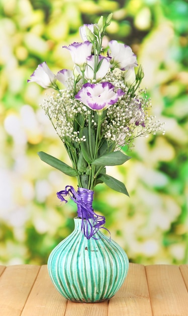 Bouquet of eustoma flowers in vase on wooden table on bright background