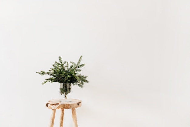 Bouquet of fir-tree branches on solid wooden stool on white