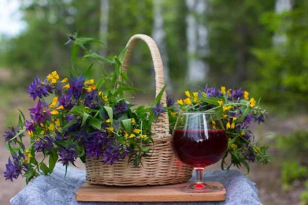 A bouquet of flowers in a basket and a glass of red wine in nature Summer still life