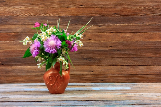 Bouquet di fiori di trifoglio, fiordalisi e gelsomino in una brocca di terracotta su un tavolo di legno