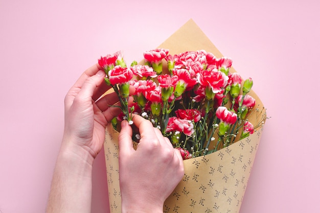 A bouquet of flowers in craft paper on a pink background. Florist holding a bouquet of fresh carnations.