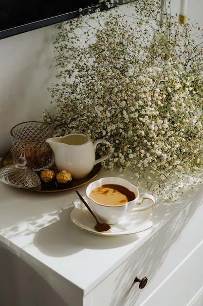 A bouquet of flowers, a cup of tea or coffee with milk and sweets on the table.