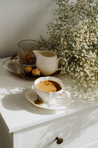 A bouquet of flowers, a cup of tea or coffee with milk and sweets on the table.