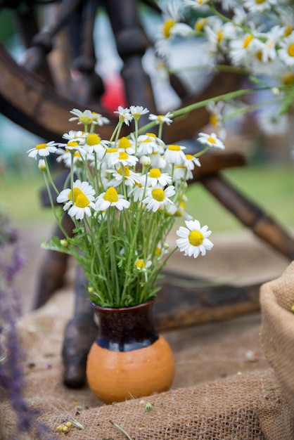 A bouquet of flowers is in a vase. Daisies are in ceramic vase handmade outdoors. Decoration at the fair - a bouquet of flowers in a ceramic vase