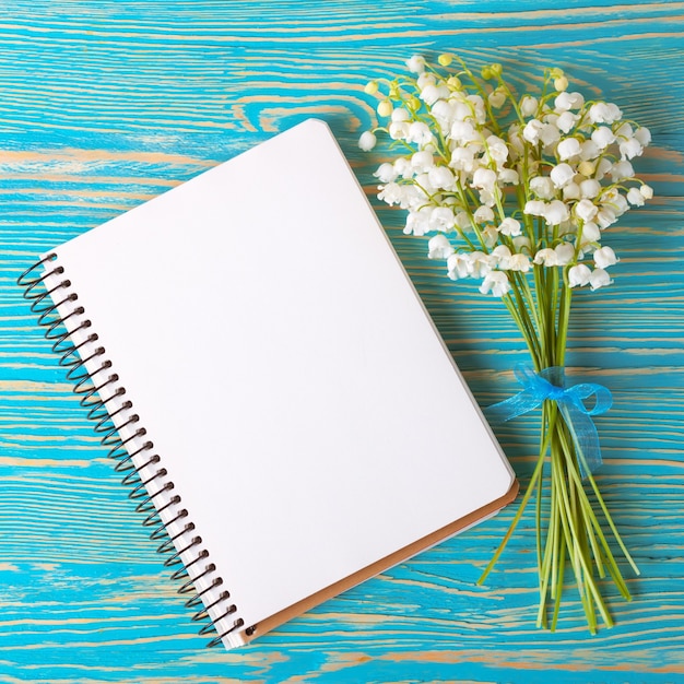 Bouquet of flowers lily of the valley and empty paper notebook on blue rustic table