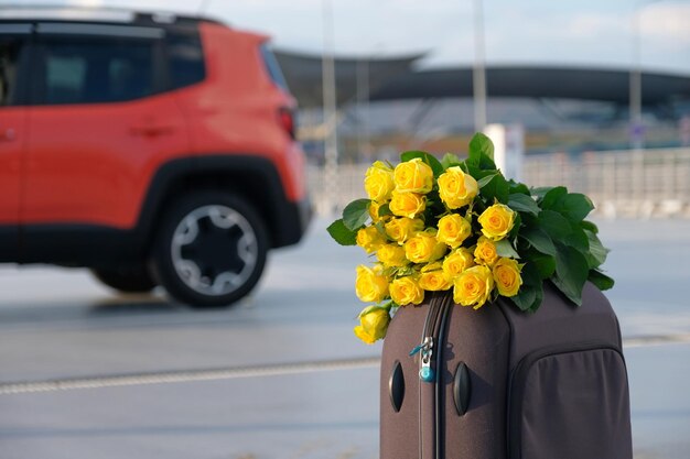 A bouquet of flowers and luggage in the parking lot against the background of a blurred car