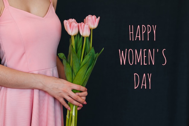 Bouquet of flowers of pink tulips in the hands of a girl. Greeting card with text Happy Women's Day