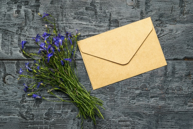 A bouquet of flowers and a postal paper envelope on a wooden table. Flat lay.