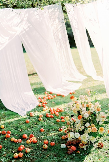Букет цветов стоит на зеленой траве среди яблок на фоне белых штор