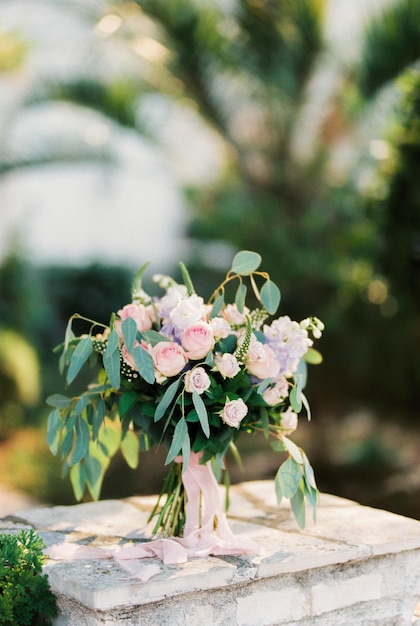 Bouquet of flowers tied with a ribbon stands on a stone fence