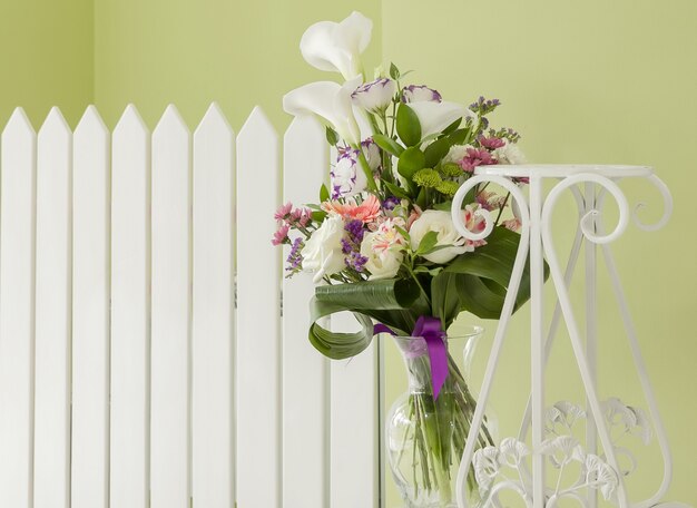 Bouquet of flowers in a vase of glass against a white fence