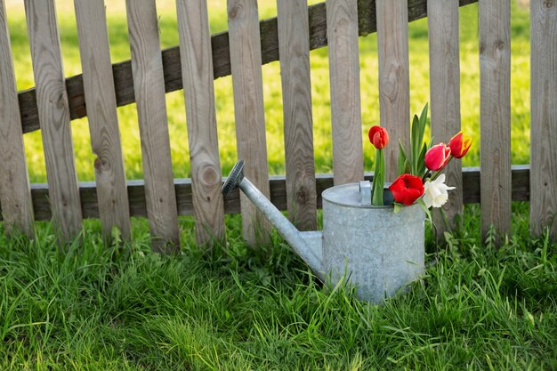 A bouquet of flowers in a watering can on an old wooden fence