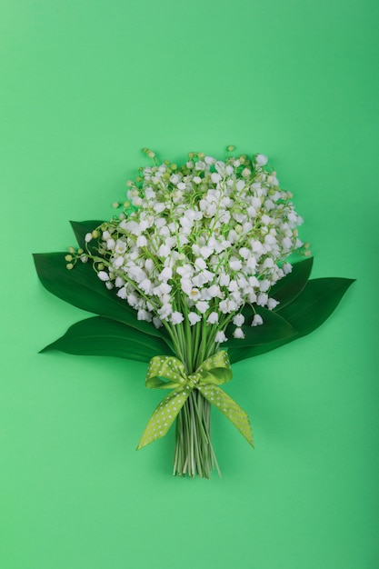 Bouquet of fragrant Lily of the valley flowers with leaves, with a green and white polka dot bow on a green background close-up