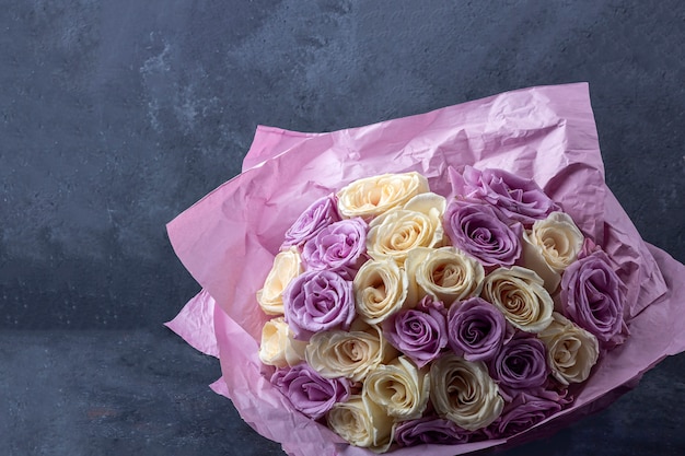 Bouquet of fresh amazing white and purple roses in craft paper on dark background