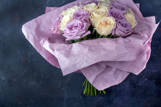 Bouquet of fresh amazing white and purple roses in craft paper on dark background