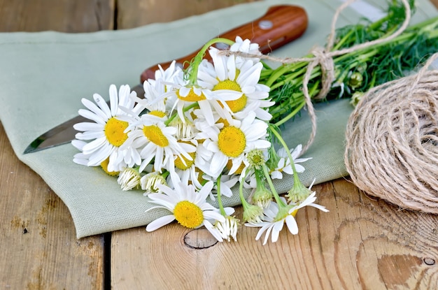 A bouquet of fresh chamomile flowers with twine and a knife on a napkin on the background of wooden boards