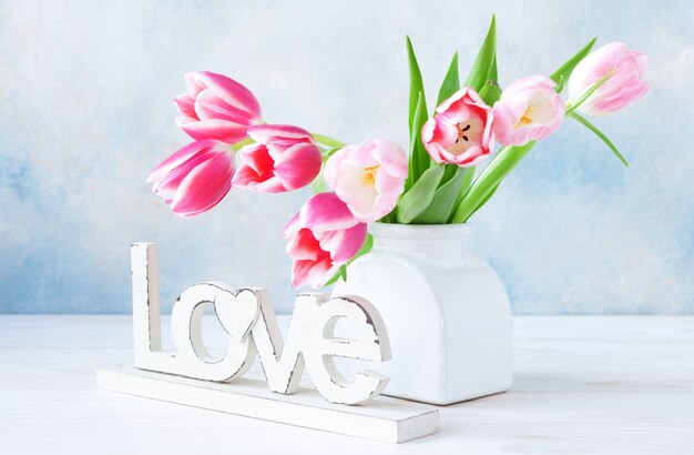 Bouquet of fresh pink tulips in vase on sky blue background