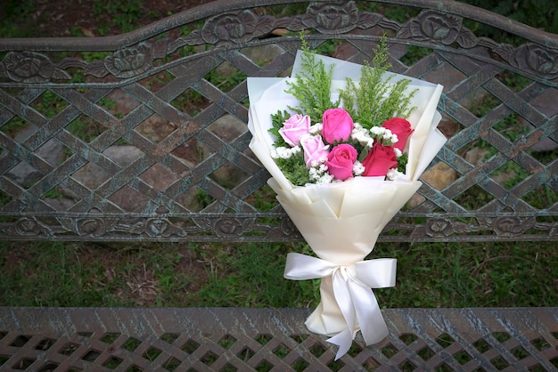 Bouquet of fresh red and pink roses rest on a rustic steel chair