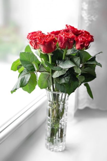 Bouquet of fresh red roses in vase stands on windowsill