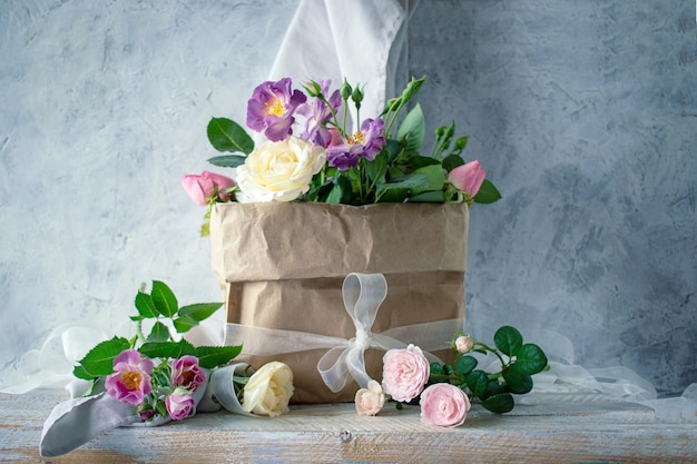 Bouquet of fresh roses in pastel shades in craft paper packaging against a gray concrete wall