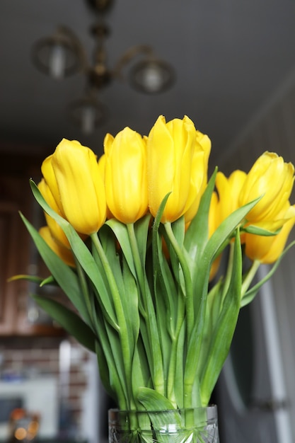 A bouquet of fresh yellow tulips in a vase on a table near the window