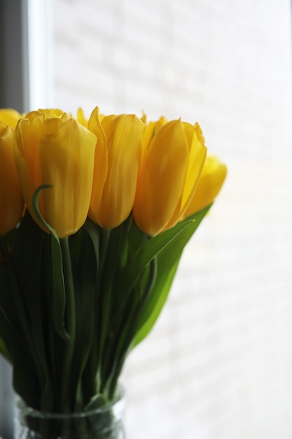 A bouquet of fresh yellow tulips in a vase on a table near the window