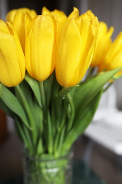 A bouquet of fresh yellow tulips in a vase on a table near the window