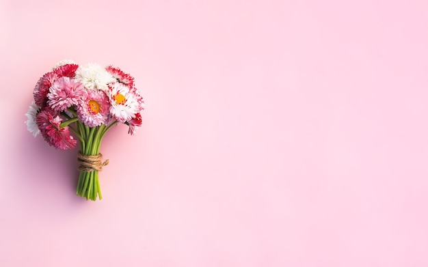 Bouquet of garden daisies with a red ribbon in a pot on a rough table. Blurred background.