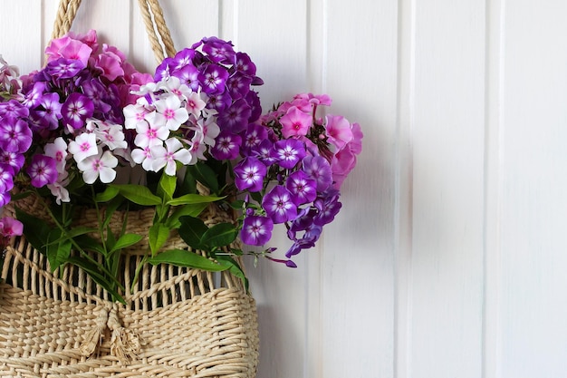 Bouquet of garden  phlox in a woven bag on a white wall  ecofriendly packaging without plastic