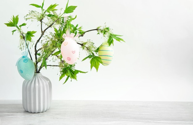 テーブルの上の花瓶に咲く新鮮な葉を持つ緑の枝の花束は、カラフルなイースターエッグで飾られています。イースターのための家のインテリアの装飾。コピースペース