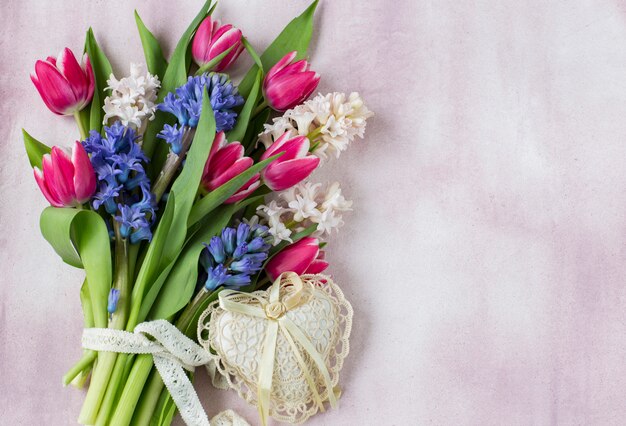 Bouquet di giacinti e tulipani e un cuore di pizzo su uno sfondo rosa