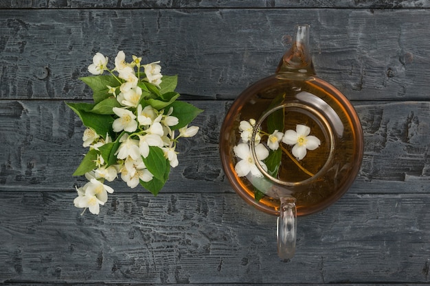 A bouquet of jasmine flowers and a teapot with floral tea on a wooden background.