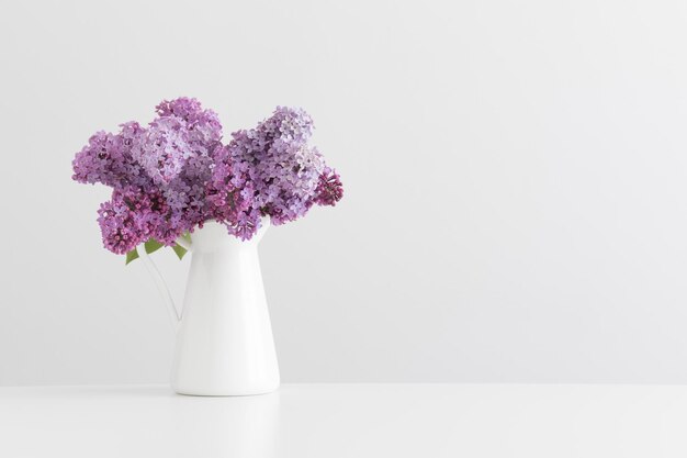 Bouquet of lilac flowers in a vase on a white table with blank copy space