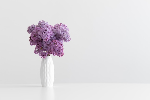 Bouquet of lilac flowers in a vase on a white table with blank copy space